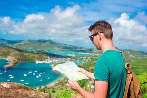 jovem turista com mapa de fundo do porto inglês de shirley heights, antígua, baía paradisíaca na ilha tropical no mar do caribe foto