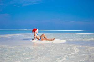 menina de chapéu de Papai Noel na praia durante as férias foto