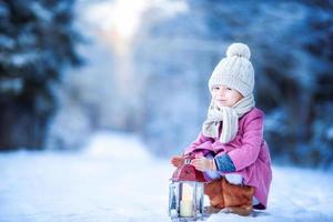 adorável menina com lanterna na floresta congelada no natal ao ar livre foto