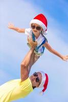 menina e pai feliz com chapéu de Papai Noel durante as férias na praia foto