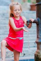 menina adorável bebendo água da torneira do lado de fora em um dia quente de verão em roma, itália foto