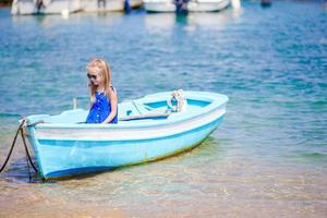 linda garota no barco azul na baía do mar, perto da cidade de mykonos, na grécia. criança gosta de nadar no pequeno barco. foto