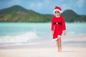 adorável menina com chapéu de Papai Noel em praia tropical foto