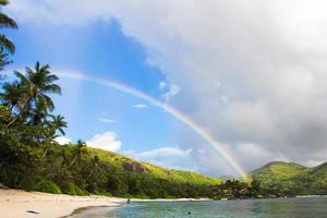 arco-íris sobre ilha tropical e praia branca em seychelles foto