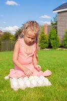 menina adorável brincando com ovos de páscoa brancos no quintal foto