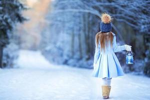 menina adorável com lâmpada e vela no inverno na véspera de natal ao ar livre foto