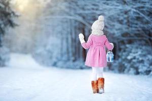 menina adorável com lâmpada e vela no inverno na véspera de natal ao ar livre foto