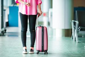 closeup luggege e passageiro de avião com passaportes e cartão de embarque e bagagem rosa em um saguão do aeroporto. jovem no aeroporto internacional andando com sua bagagem. foto