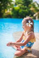 menina adorável com flor atrás da orelha senta-se perto da piscina foto