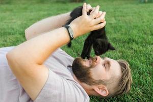 close-up do homem com o gatinho deitado e brincando na grama - animais de amor de amizade e conceito de dono de animal de estimação foto