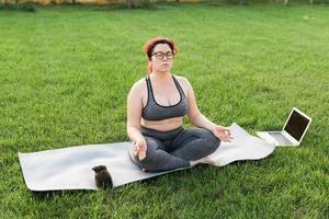 mulher de positividade corporal plus size fazendo meditação no tapete de ioga com gatinho no quintal - conceito de bem-estar e saúde mental foto