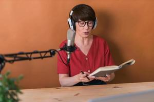 mulher madura fazendo gravação de podcast para seu show online. mulher de negócios atraente usando fones de ouvido na frente do microfone para uma transmissão de rádio foto