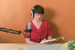 apresentadora de rádio feminina de meia-idade falando no microfone e lendo notícias - conceito on-line de transmissão de rádio foto