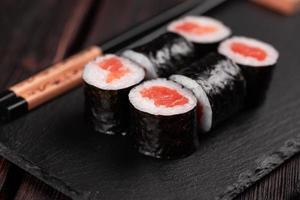 rolo de sushi maki com abacate salmão e caviar tobiko servido em close-up de placa preta - comida japonesa foto