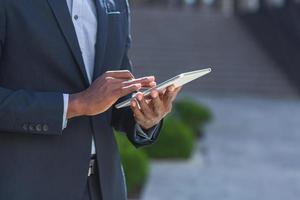 feche as mãos do empresário americano afro usando o tablet. um homem de negócios negro em um terno formal foto