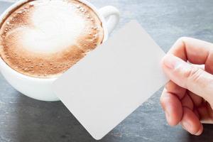 pessoa segurando um cartão de visita em branco com um café com leite foto