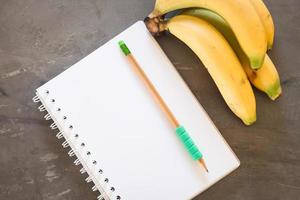 caderno com um lápis verde e bananas foto