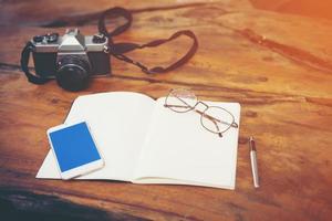 câmera vintage com notebook, telefone e óculos na mesa de madeira foto