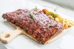 Costelas grelhadas para churrasco com legumes e batatas fritas na tábua de madeira foto