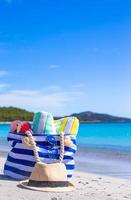 bolsa azul, chapéu de palha, chinelos e toalha na praia branca foto