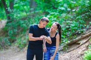 jovem casal ativo olhando para o monitor de frequência cardíaca do relógio inteligente tendo uma pausa enquanto corre na floresta foto