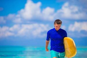 surfista jovem feliz na praia branca com prancha de surf amarela foto