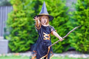 adorável menina vestindo fantasia de bruxa no halloween ao ar livre. doçura ou travessura. foto