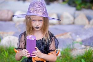 halloween e adorável garotinha com vela vestida de bruxa foto