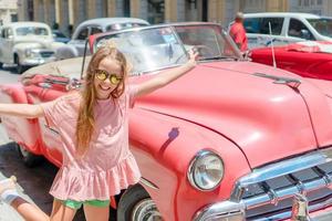 menina adorável na área popular em velha havana, cuba. retrato de criança fundo clássico carro americano clássico foto