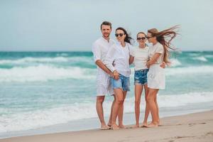 família de pais jovens e dois filhos sorrindo e aproveitando o tempo juntos nas férias na praia foto