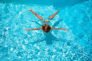 menina bonita e feliz nadando na piscina ao ar livre como uma estrela foto
