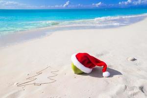 desenho de abeto na areia branca da praia com chapéu vermelho de papai noel foto