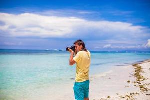 jovem fotografando com a câmera nas mãos em uma praia tropical foto