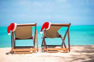 natal na praia - espreguiçadeiras com chapéus de papai noel no mar. conceito de férias de natal foto