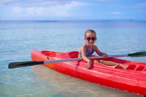 corajosa menina bonitinha flutuando em um caiaque no alto mar azul foto