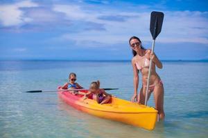 duas crianças pequenas e uma jovem mãe andando de caiaque no oceano azul tropical foto