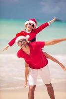 pai e filha com chapéu de Papai Noel se divertem na praia tropical foto