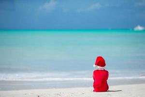 adorável menina com chapéu de Papai Noel em praia tropical foto