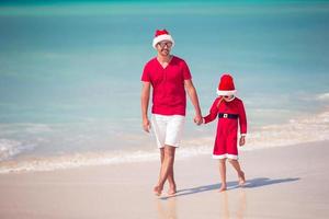 pai e filha com chapéu de Papai Noel se divertem na praia tropical foto