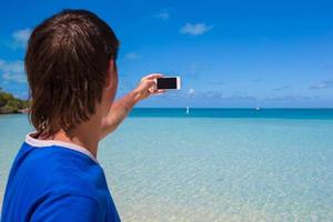 jovem de chapéu de Papai Noel com telefone na praia tropical do Caribe foto