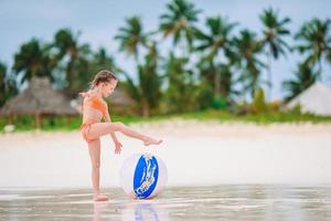 adorável menina brincando na praia com bola foto