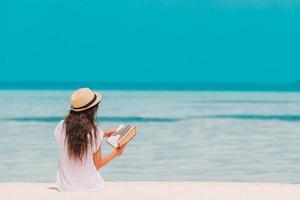 retrato de uma jovem mulher relaxando na praia, lendo um livro foto