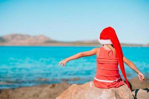 adorável menina com chapéu de Papai Noel em praia tropical foto