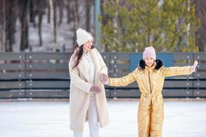 menina adorável com sua mãe patinando na pista de gelo foto
