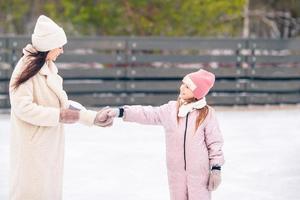 menina adorável com sua mãe patinando na pista de gelo foto