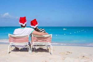 vista traseira do jovem casal em chapéus de Papai Noel desfrutar de férias na praia foto