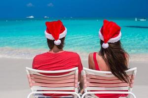 casal romântico feliz em chapéus de papai noel vermelhos na praia tropical foto