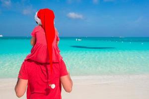 pai e filha com chapéu de Papai Noel na praia tropical foto