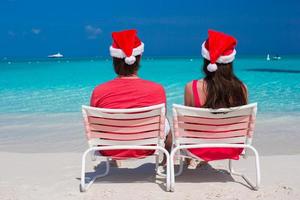 casal romântico feliz em chapéus de papai noel vermelhos na praia tropical foto