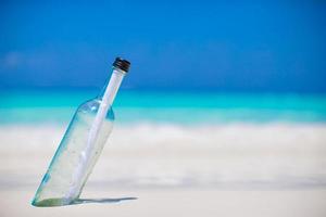 garrafa com mensagem enterrada na areia branca foto
